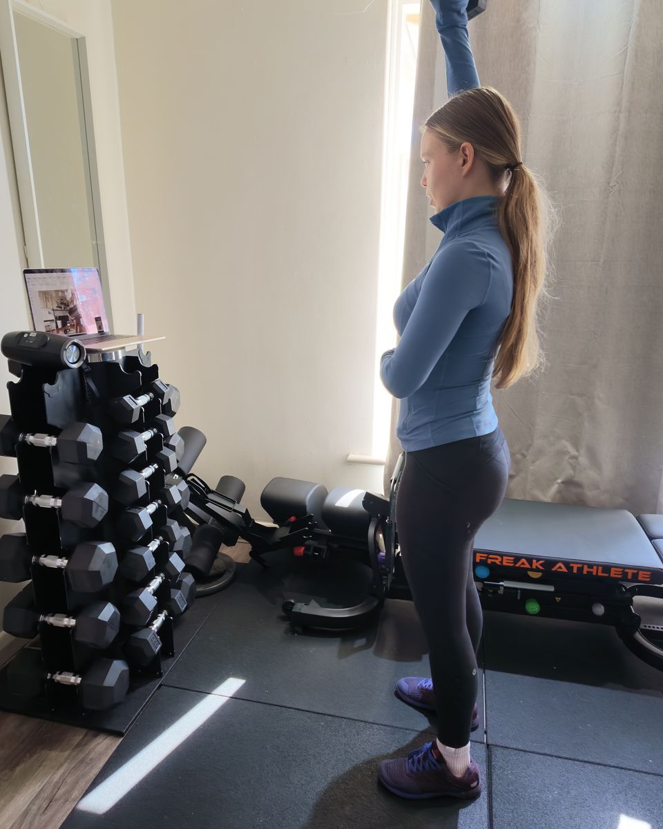 Liubov coaching a live online session from her home studio, laptop on the dumbbell rack